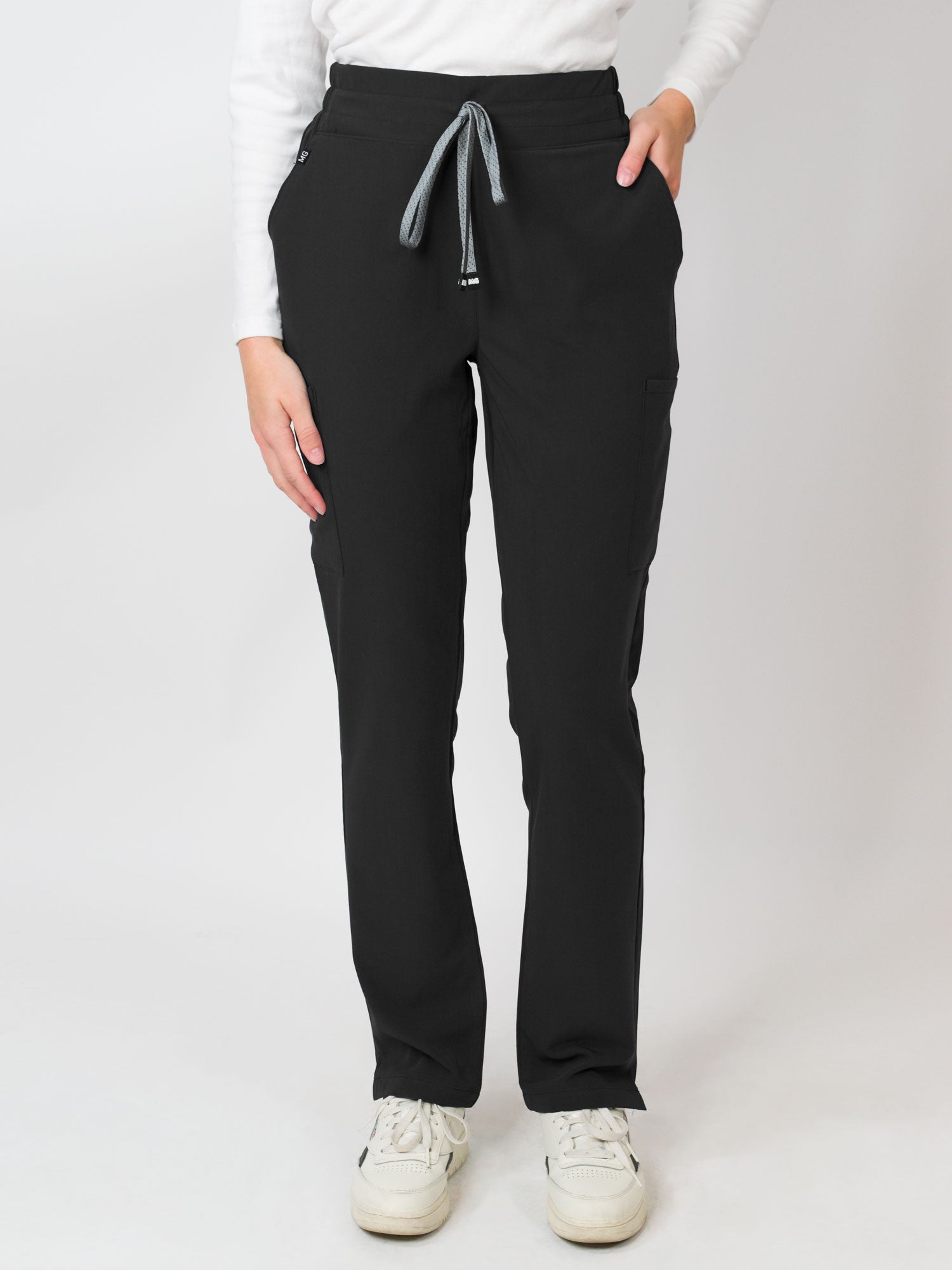 A woman standing, wearing navy mid-rise slim straight scrub pants with an adjustable drawstring and multiple pockets.