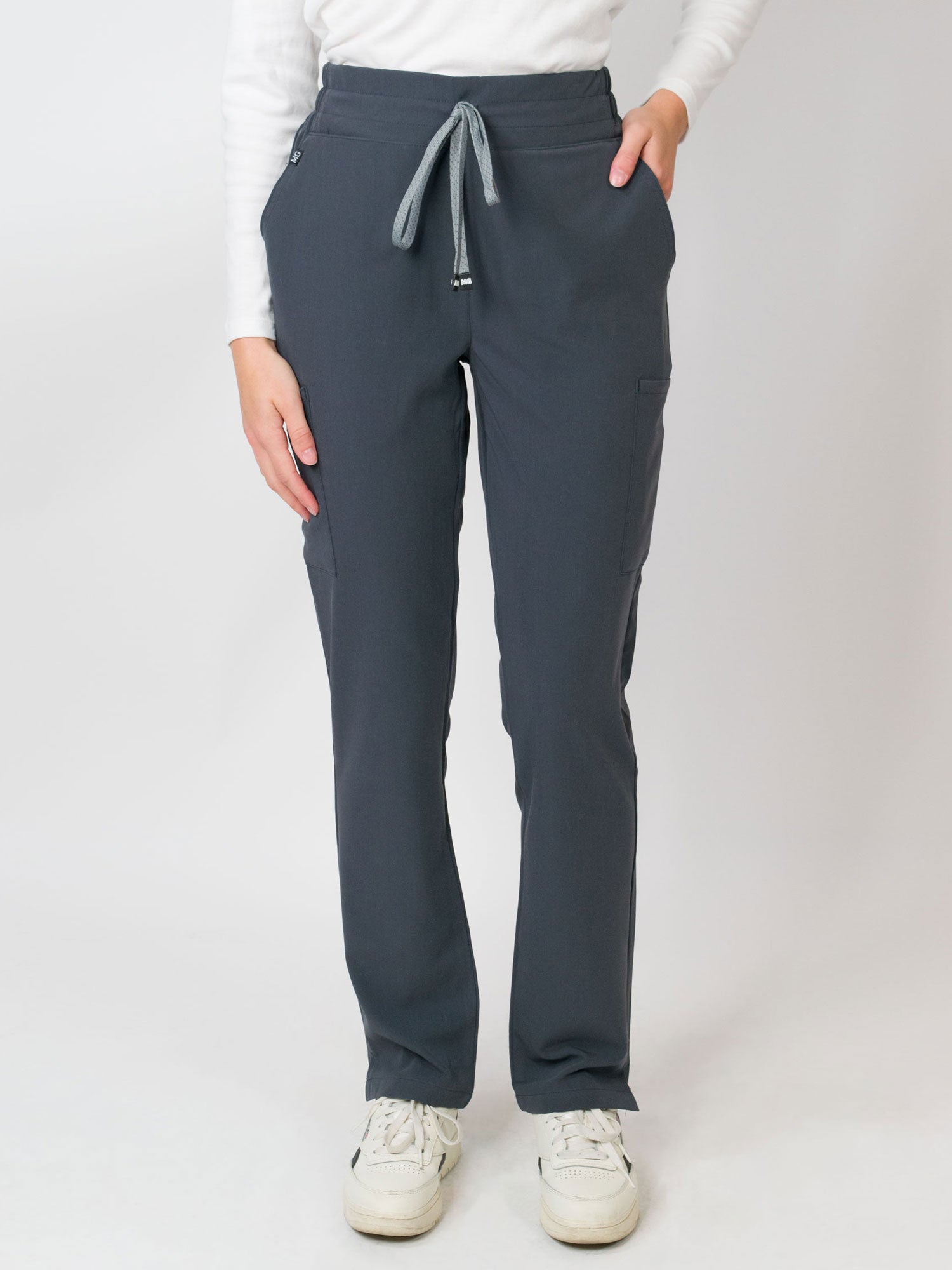 A woman wearing navy mid-rise slim straight scrub pants with an adjustable drawstring and multiple pockets, with Medgear branding.
