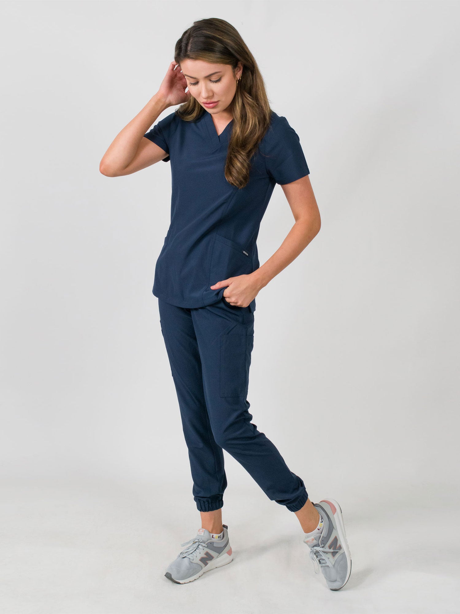 Woman modeling a women's medical scrub set with a V-neck top and jogger pants in navy blue color, featuring multiple pockets.