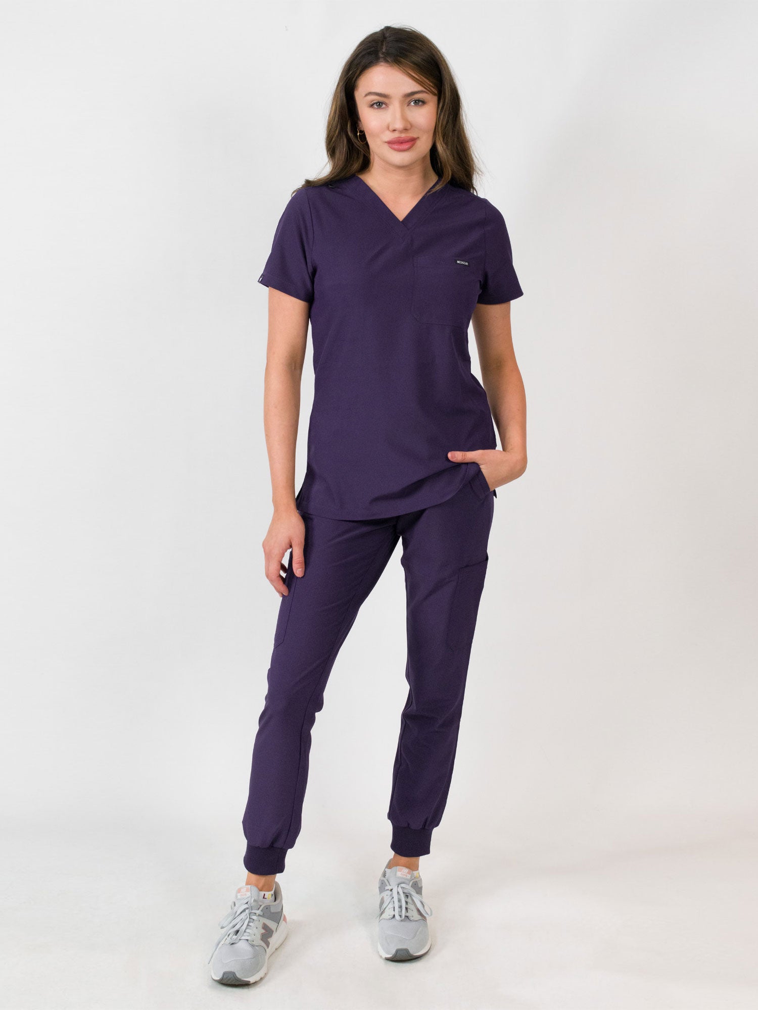 Woman modeling a purple medical scrub set with a V-neck top and jogger scrub pants