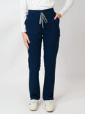 A woman standing, wearing navy mid-rise slim straight scrub pants with an adjustable drawstring and multiple pockets.