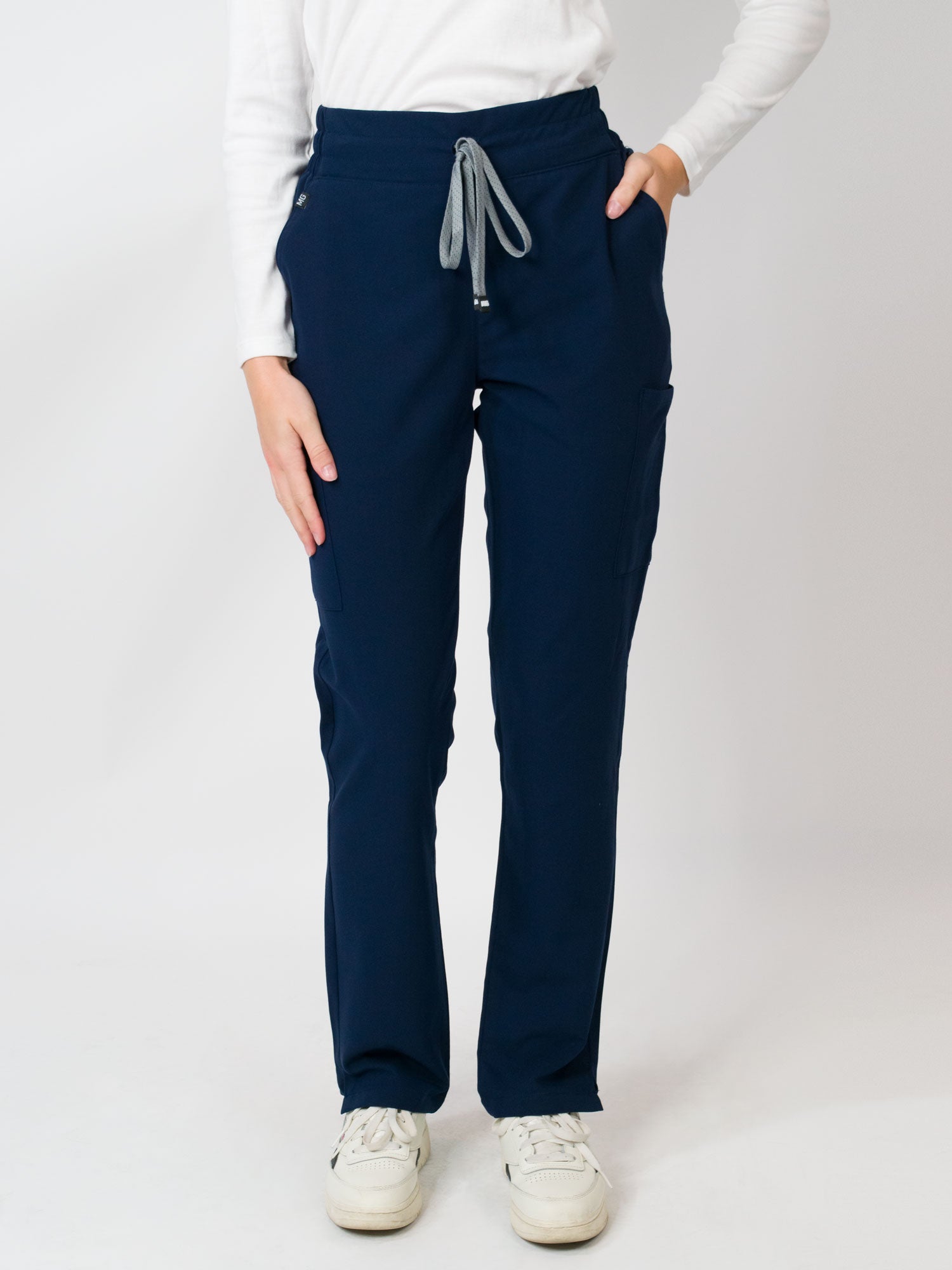 A woman standing, wearing navy mid-rise slim straight scrub pants with an adjustable drawstring and multiple pockets.