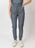 A woman standing in a three-quarter pose wearing gray mid-rise slim jogger scrub pants with an elastic waistband and drawstring, with multiple pockets.