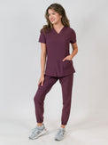 Woman modeling a women's medical scrub set with a V-neck top and jogger pants in purple color, featuring multiple pockets.