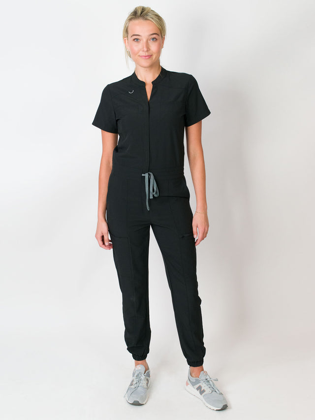 Black Medgear scrub jumpsuit with a mandarin collar, short sleeves, and elastic jogger cuffs. The jumpsuit has multiple pockets and a zipper front.