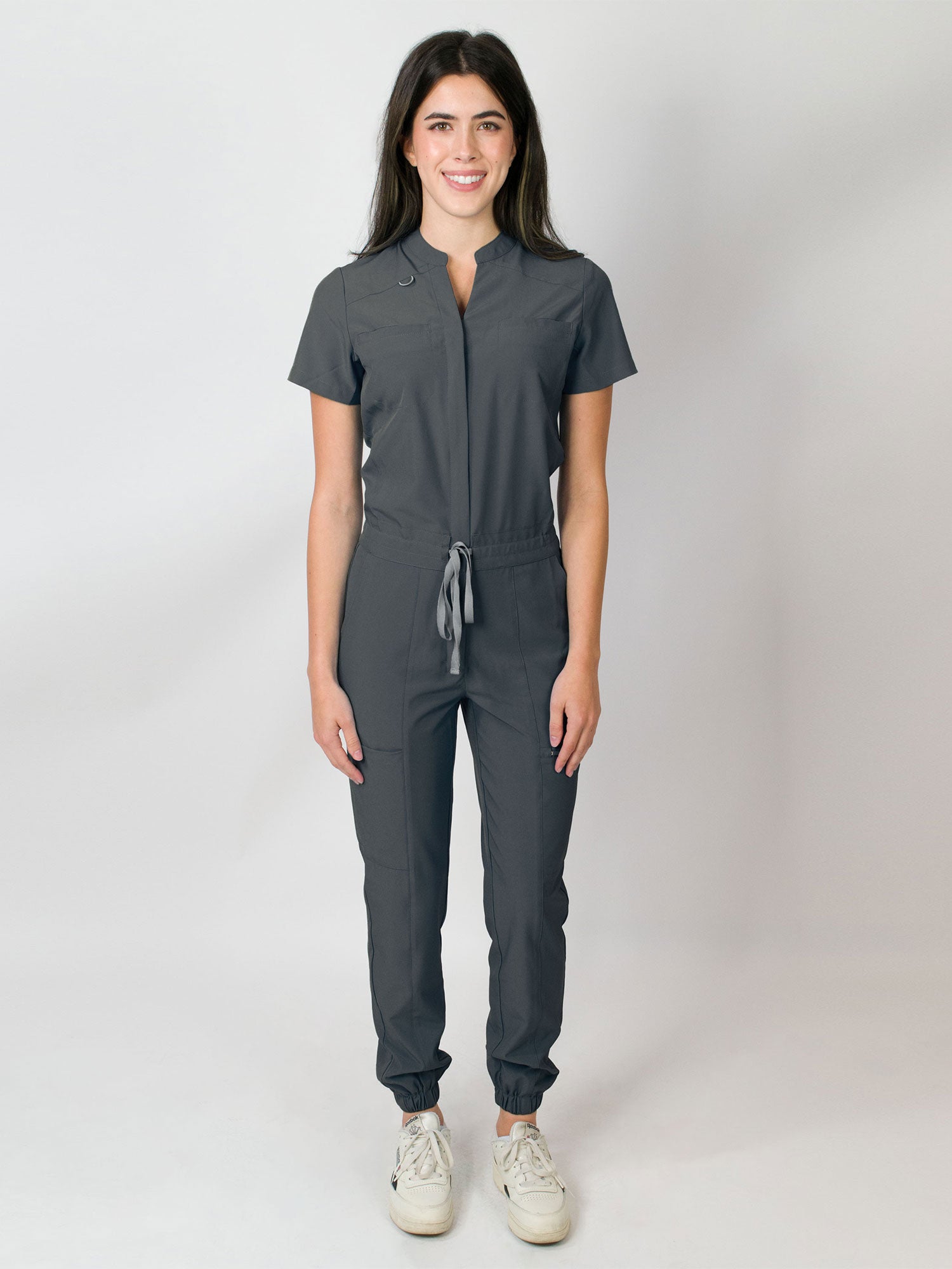 Grey scrub jumpsuit with a mandarin collar, short sleeves, and elastic jogger cuffs. The jumpsuit has multiple pockets and a zipper front.