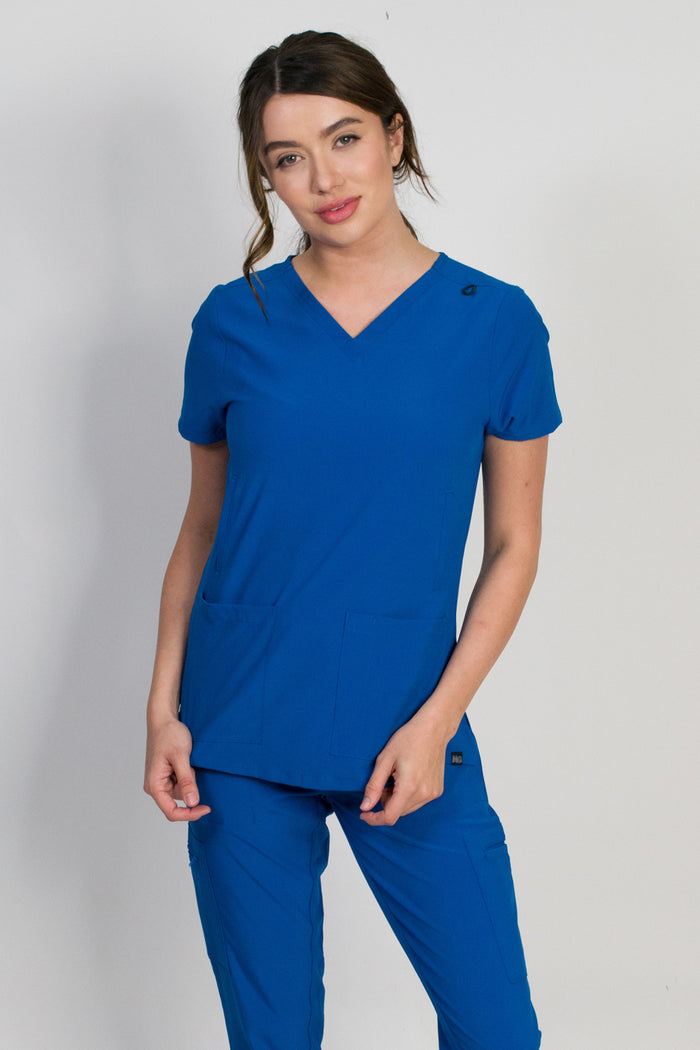A woman wearing a royal blue-colored scrub top with a V-neckline and 5 functional pockets, including handwarmers and patch pockets.