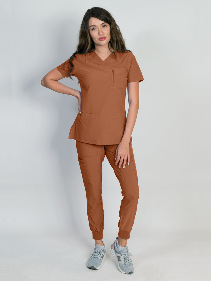 Scrub set in mocha color with a mitered neck V-neck top and jogger pants, both with multiple pockets, made from a smooth stretch fabric.
