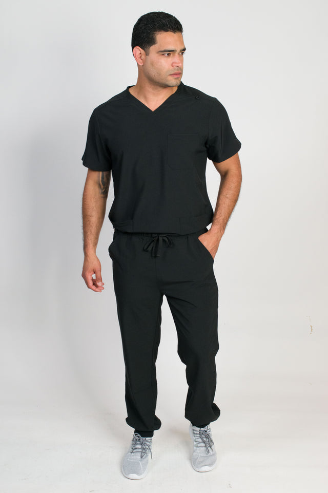A man wearing a black V-neck scrub set with 4 pockets and rib knit cuffs. The set includes a top with a chest patch pocket and bottom hem pockets, along with matching pants with inset trouser pockets and back welt pockets.