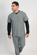 A man wearing a heather grey V-neck scrub set with 4 pockets and rib knit cuffs. The set includes a top with a chest patch pocket and bottom hem pockets, along with matching pants with inset trouser pockets and back welt pockets.